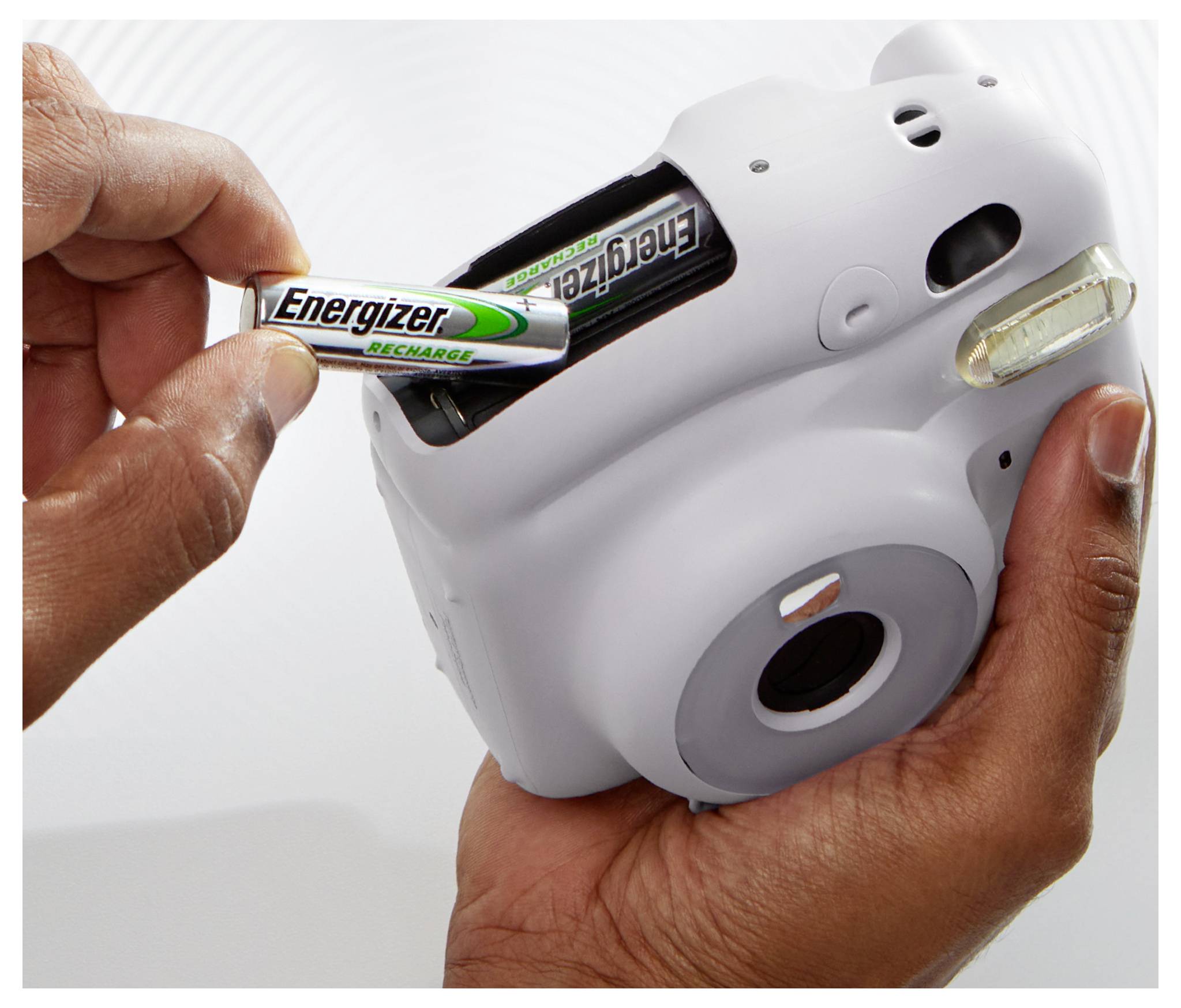 'Two hands are inserting an Energizer battery into a white, compact camera.'