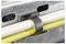 A black cable clamp secures two parallel cables, one white and one yellow, to a metal surface with elongated holes on its side.