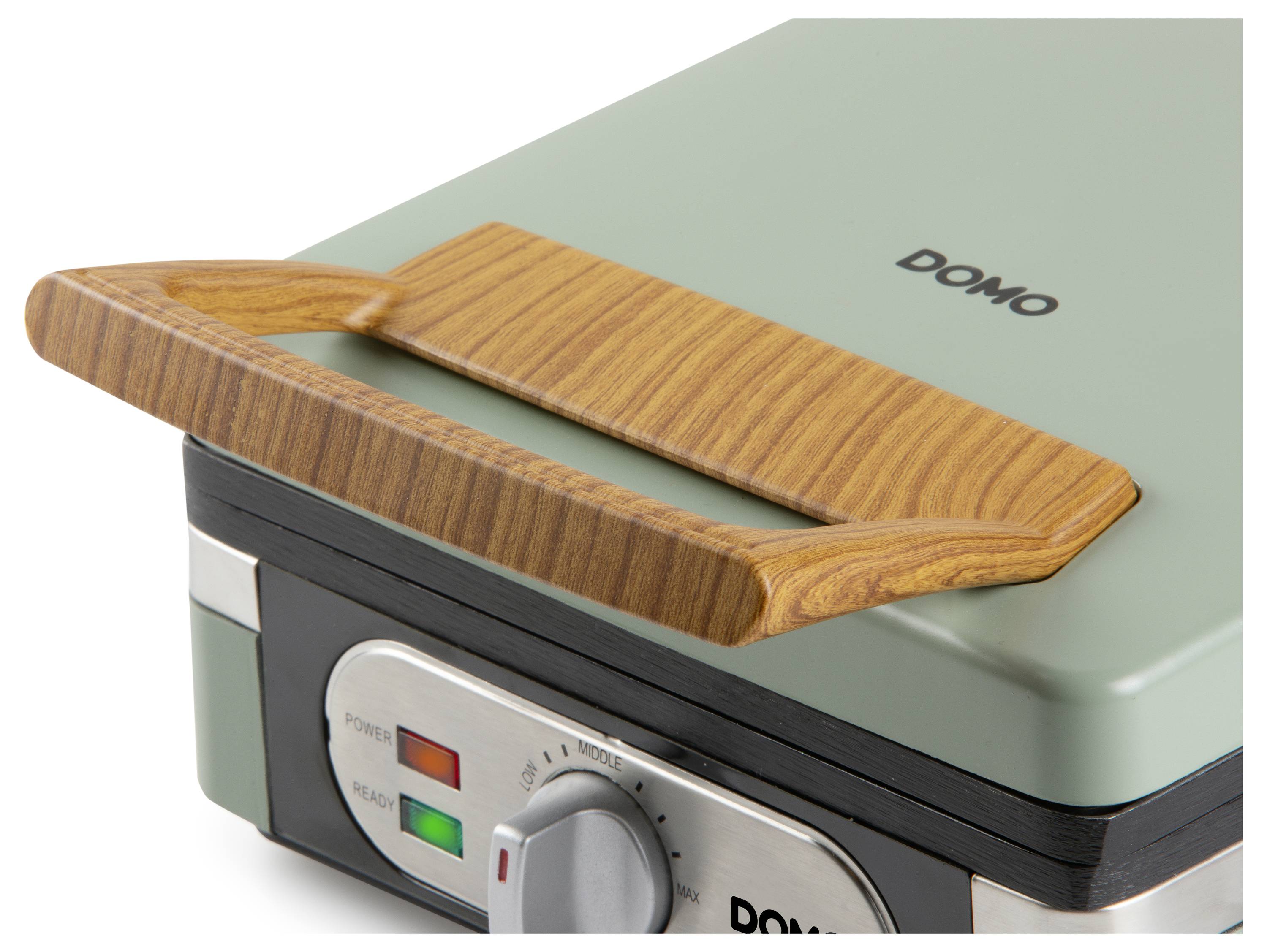 A close-up of a green sandwich maker with a wooden handle, showing power and ready indicator lights and a temperature control knob.