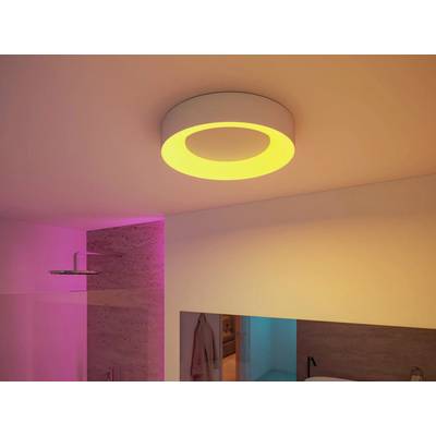 A modern bathroom features a circular ceiling light emitting a warm glow. The room is softly lit with pink and yellow tones.