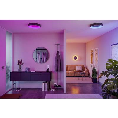 A modern living space with pink and purple ambient lighting, featuring a hallway with a coat rack and console table, leading to a cozy seating area.