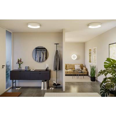 Modern living room and hallway with minimalist decor. Hallway features a dark console, mirror, and coat rack. Living area has a beige sofa, plants, and wall art.