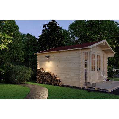Wooden cabin with red roof, surrounded by greenery and lit by an outdoor light. Firewood stacked by the wall; a path leads to the door.