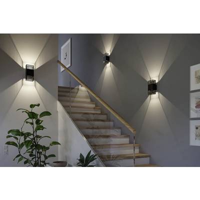 'A staircase with wooden steps is illuminated by three modern wall lights. There is a plant at the bottom and framed artwork on the wall.'