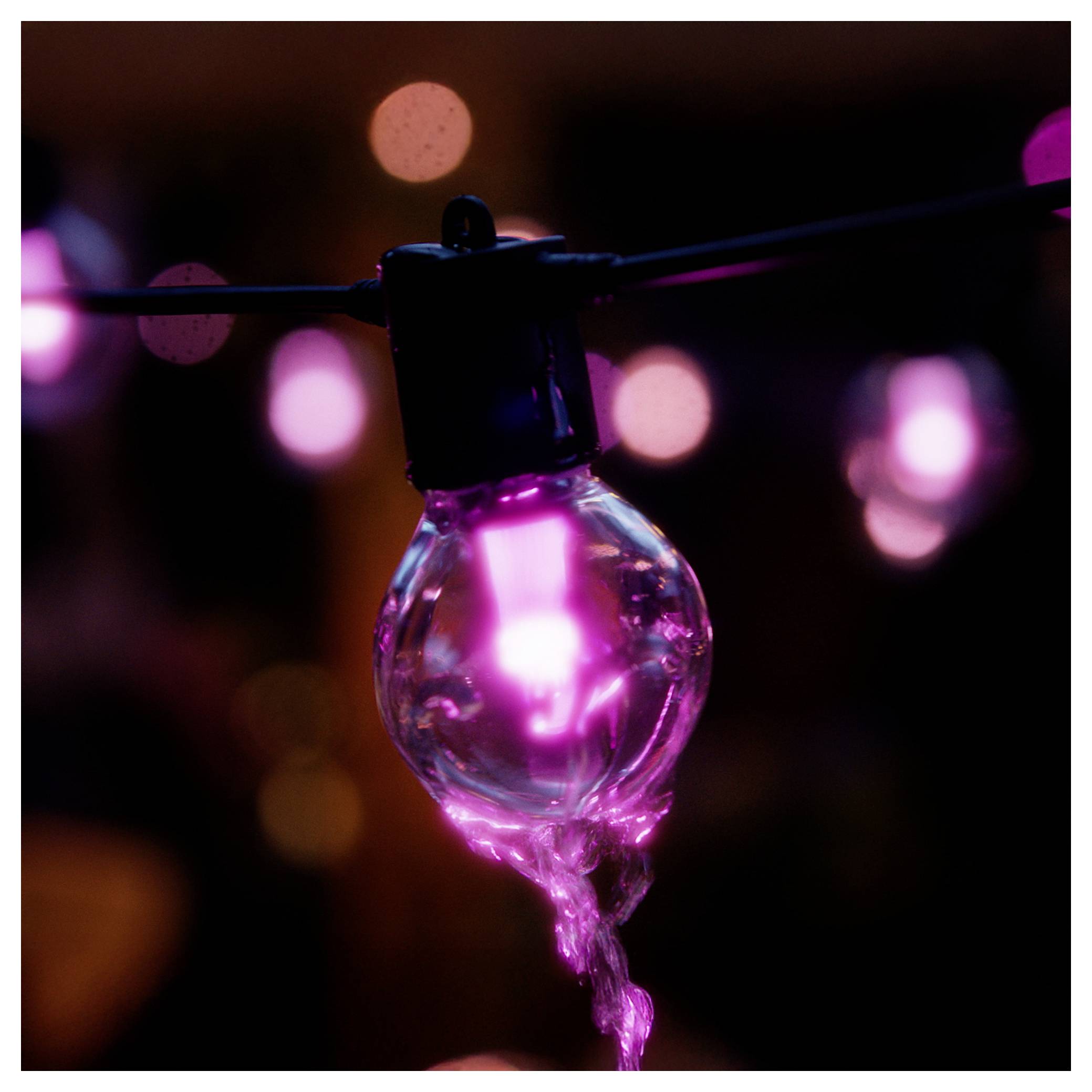 A close-up of a glowing pink bulb hanging from a wire, with blurred pink and orange lights in the background, creating a warm atmosphere.
