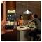 A person adjusts a smart home lighting app on a phone, changing the dining room's ambiance, where two people enjoy a meal together.