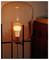 A lit, modern bulb in a glass lamp on a metal stand, casting a warm glow; placed beside a wooden cabinet, creating a cozy ambiance.