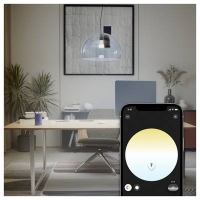A modern office with a wooden desk, chair, and plants. A smartphone displays a light control app with a gradient circle for adjusting brightness.