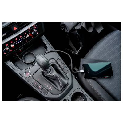 A mobile phone is charging in a car's interior. The phone is connected via a cable to the car's central console near the gear shift.