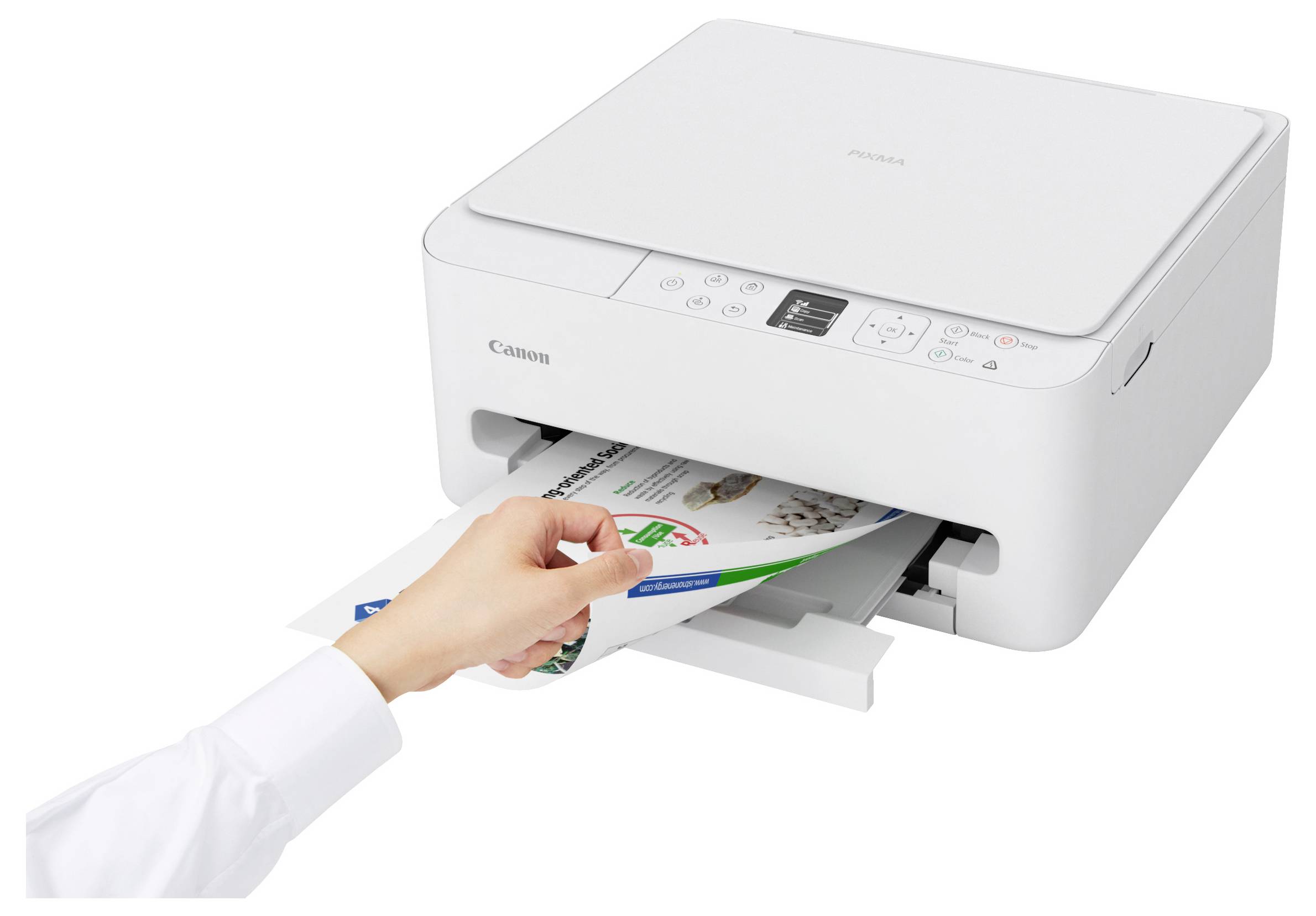 A person retrieves printed sheets from a Canon printer. The printer is white and compact, with visible control buttons on the top panel.