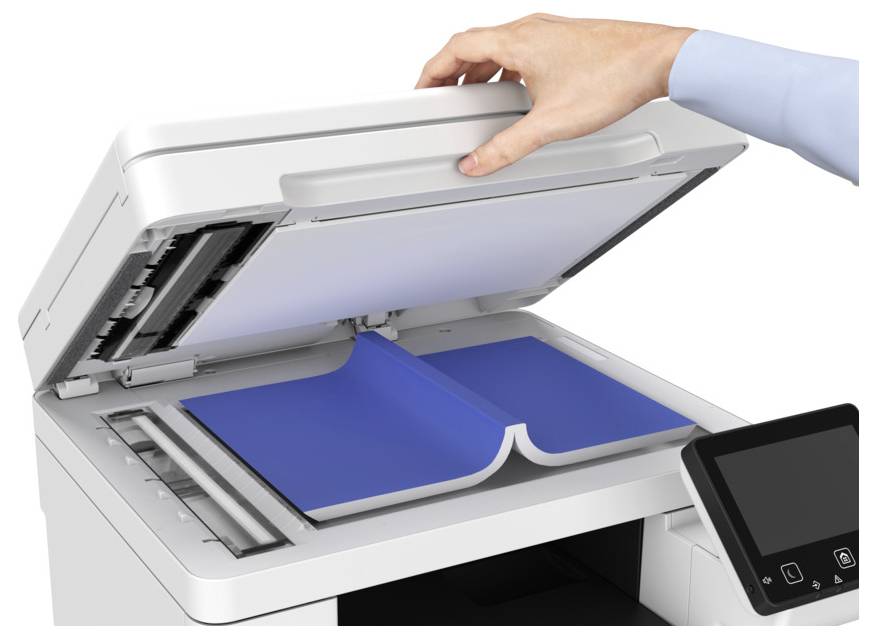 A person’s hand lifts the lid of a photocopier, revealing an open book placed on the scanning surface, ready for copying.