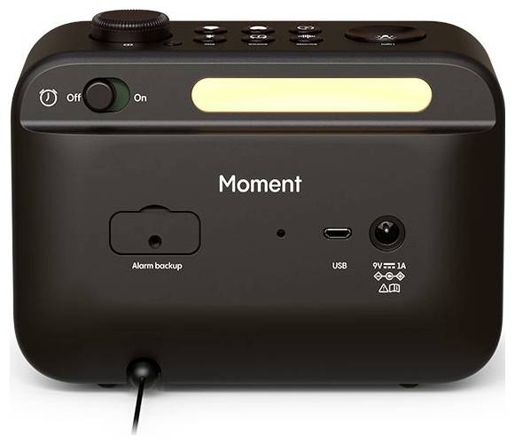 A black digital alarm clock with 'Moment' branding, featuring an on/off switch, USB port, and an illuminated display on top.