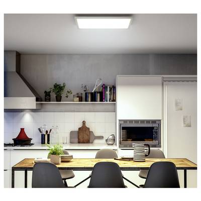 A modern kitchen with a wooden table set for dining, chairs, plants, and cooking utensils on shelves. A wall oven and books are visible.