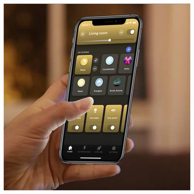 Person holding a smartphone showing a smart home app interface with various lighting presets for the living room, such as 'Relax' and 'Concentrate'.