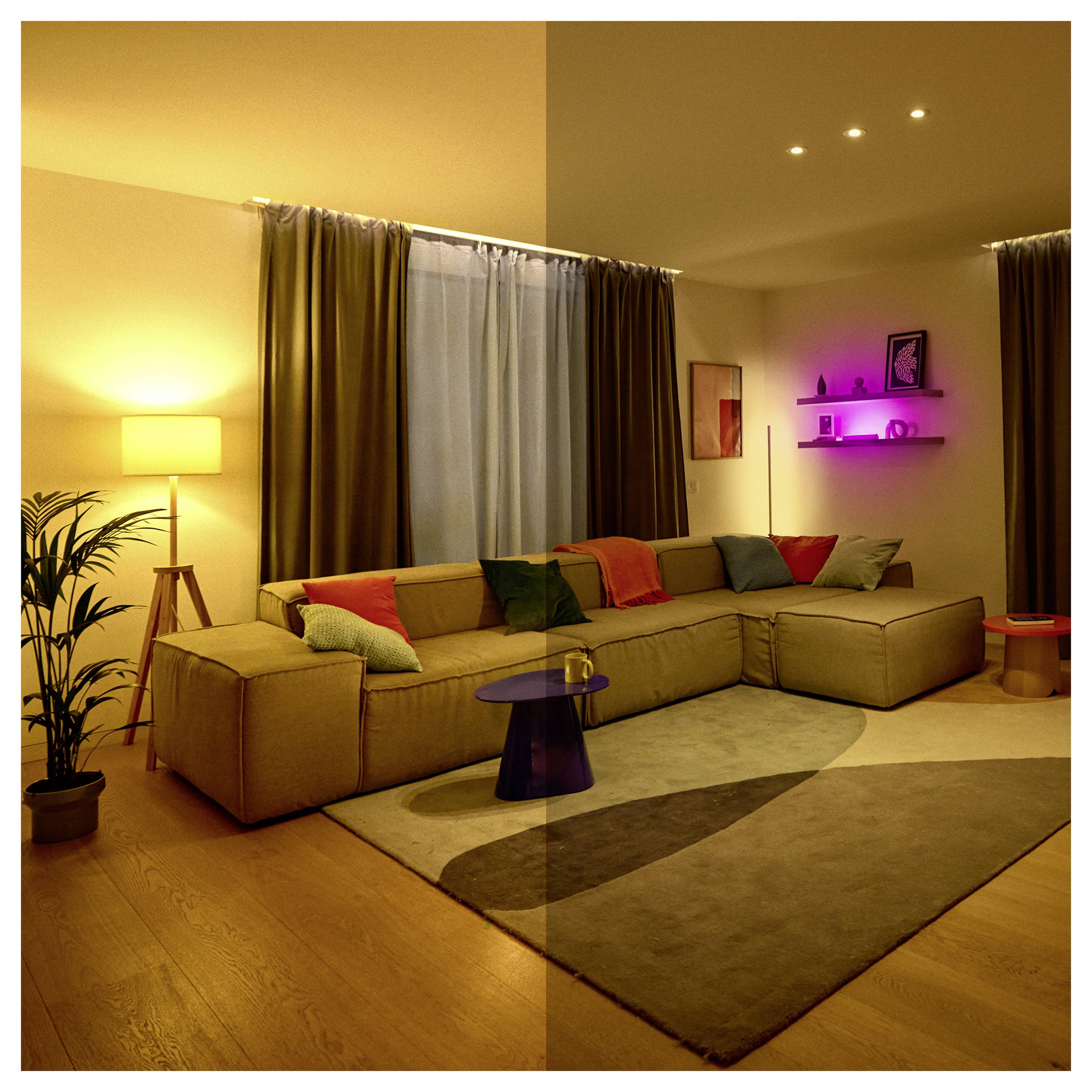 A cozy living room with a sectional sofa, pillows, standing lamp, and potted plant. Shelves with pink accent lighting add ambiance.