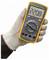 A gloved hand holds a digital multimeter displaying '220.8 V AC'. The device has a dial for different settings and various buttons.