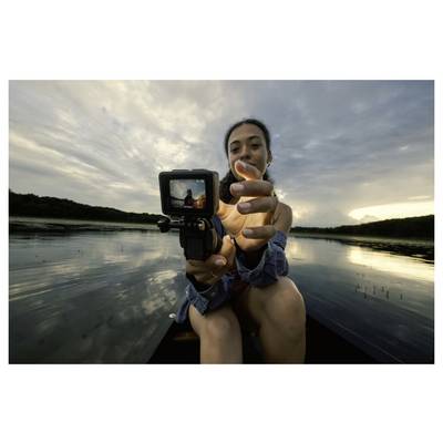 A person in a boat holds a camera, showing a view of the lake and cloudy sky behind. The scene is captured on the camera's screen.