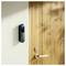 A smart doorbell installed on a wall beside a wooden door, featuring a camera and button.