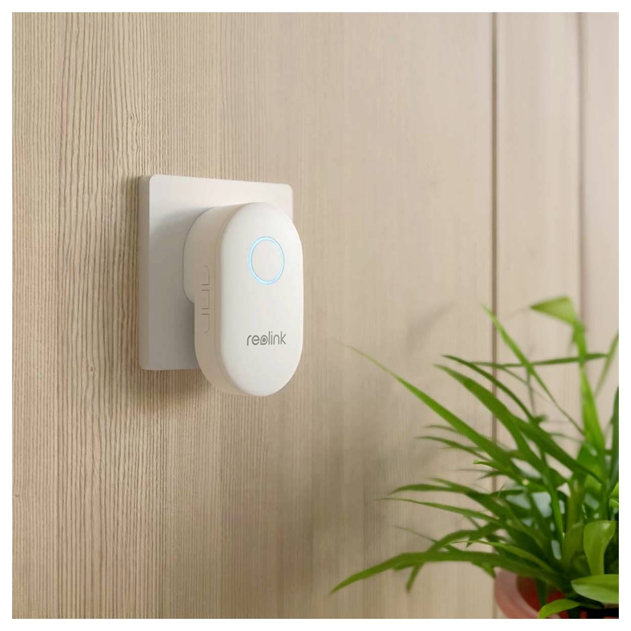 A white, wall-mounted security camera with a blue light and 'reolink' branding, next to a green potted plant on a wooden wall.