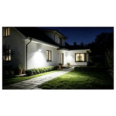 Nighttime exterior of a modern house with lit windows, a stone walkway, and a neatly landscaped lawn and shrubs.