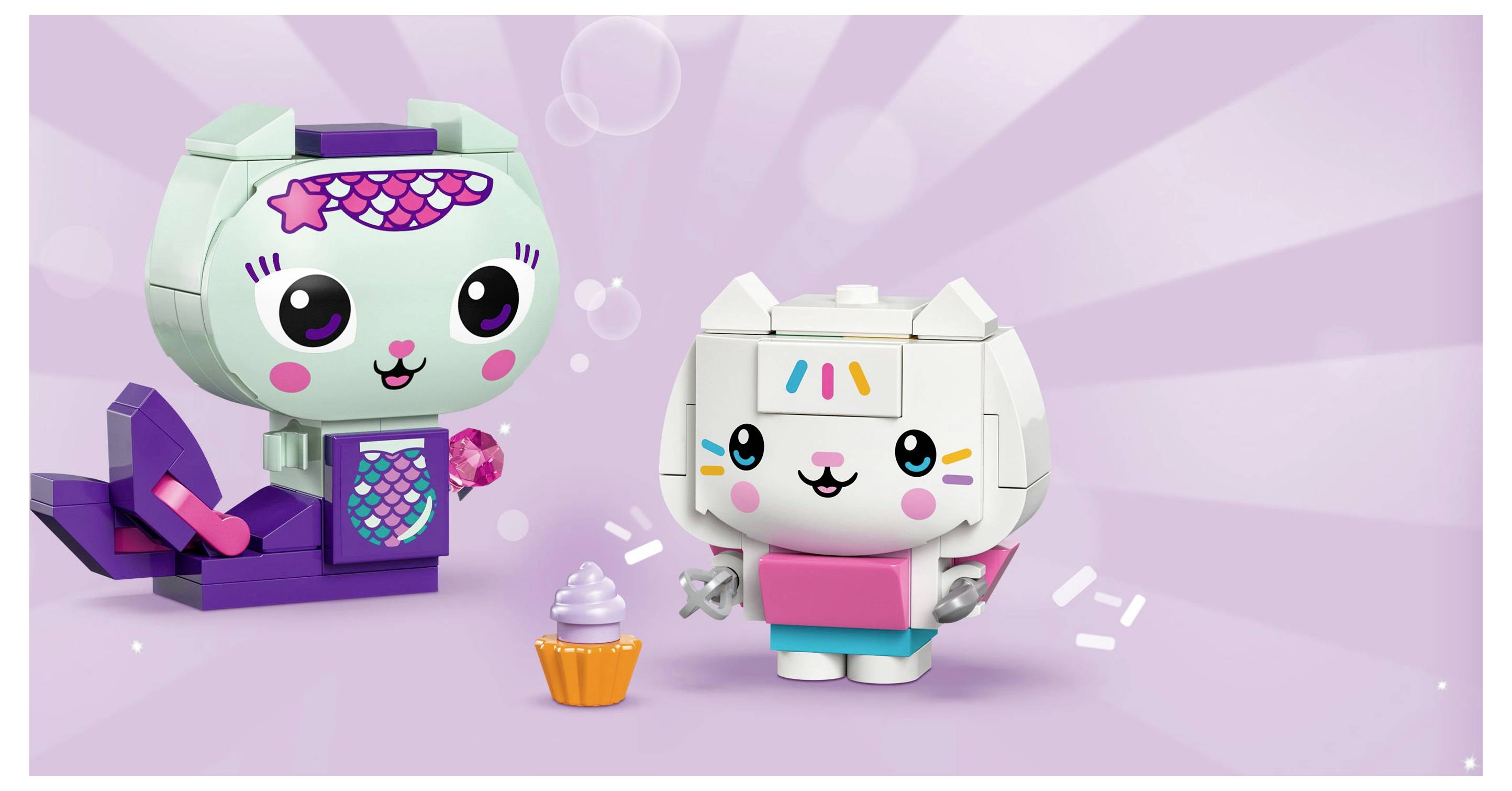 Two colorful, block-like toy figures resembling animals with happy expressions stand on a purple background. One holds a cupcake.
