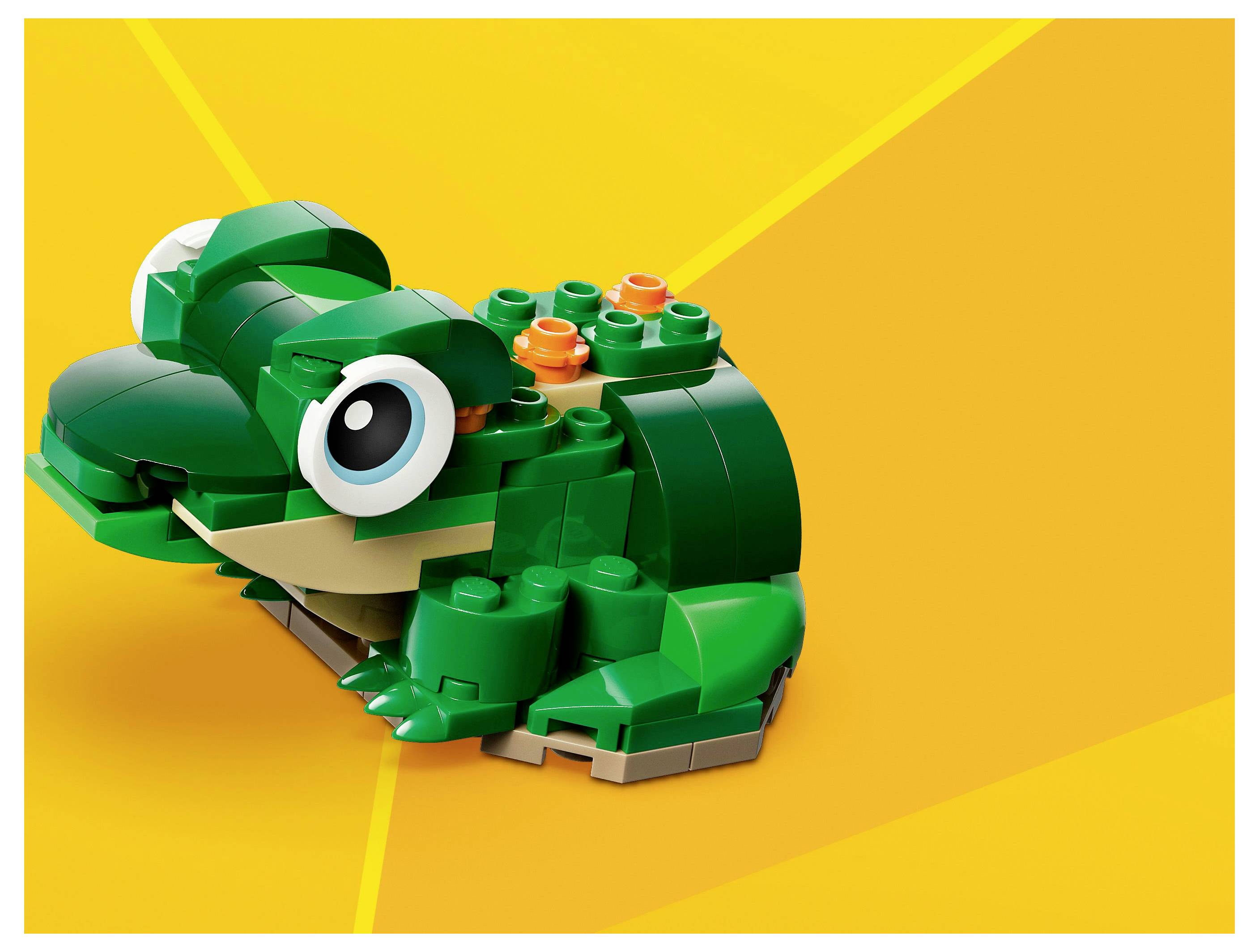 A green toy frog made of building blocks on an orange background, with big, cartoonish eyes and a smiling mouth.