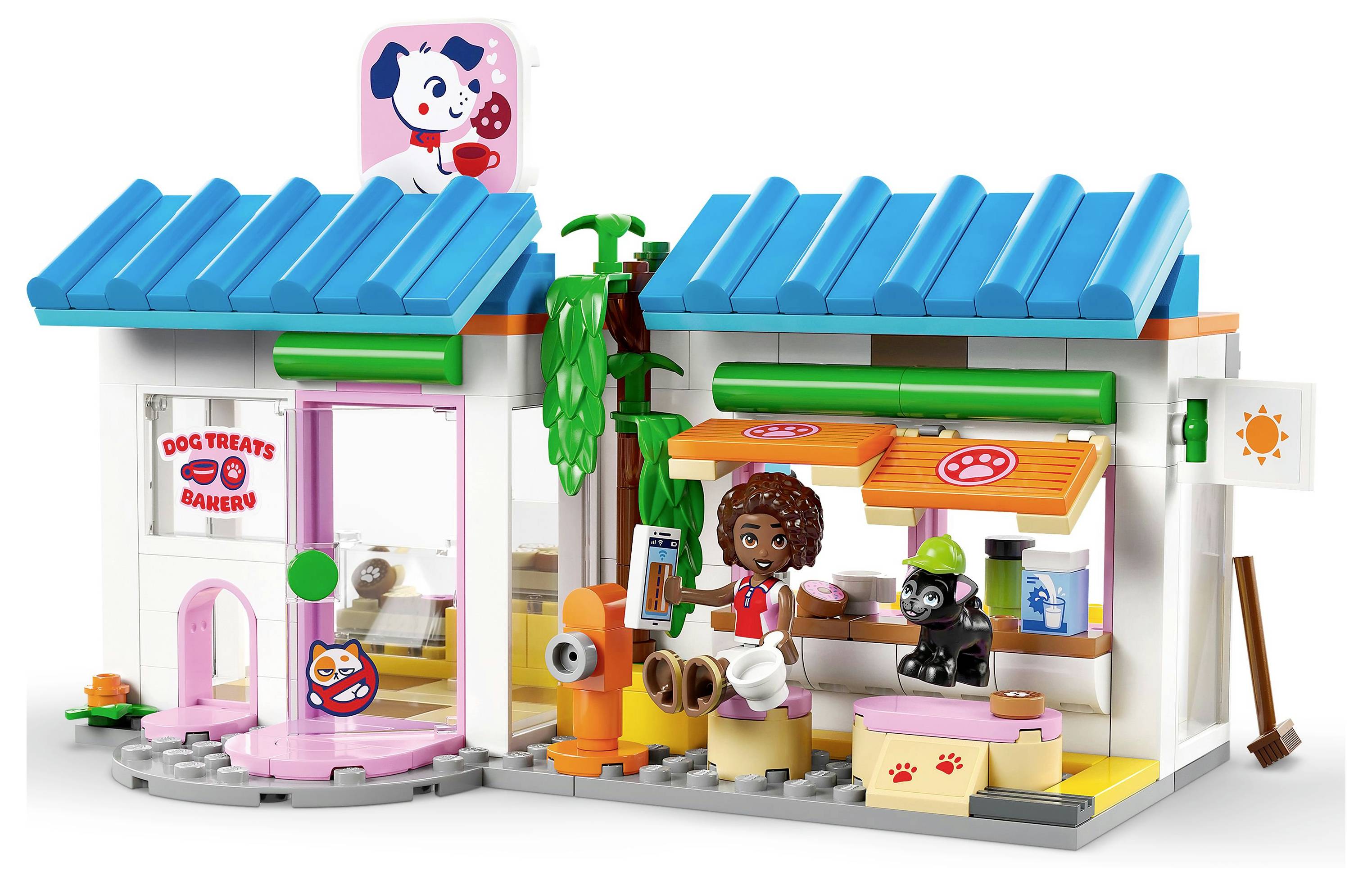 Lego set depicting a colorful dog treat bakery with two minifigures, a dog, bakery items, and a tree, showing a playful scene.