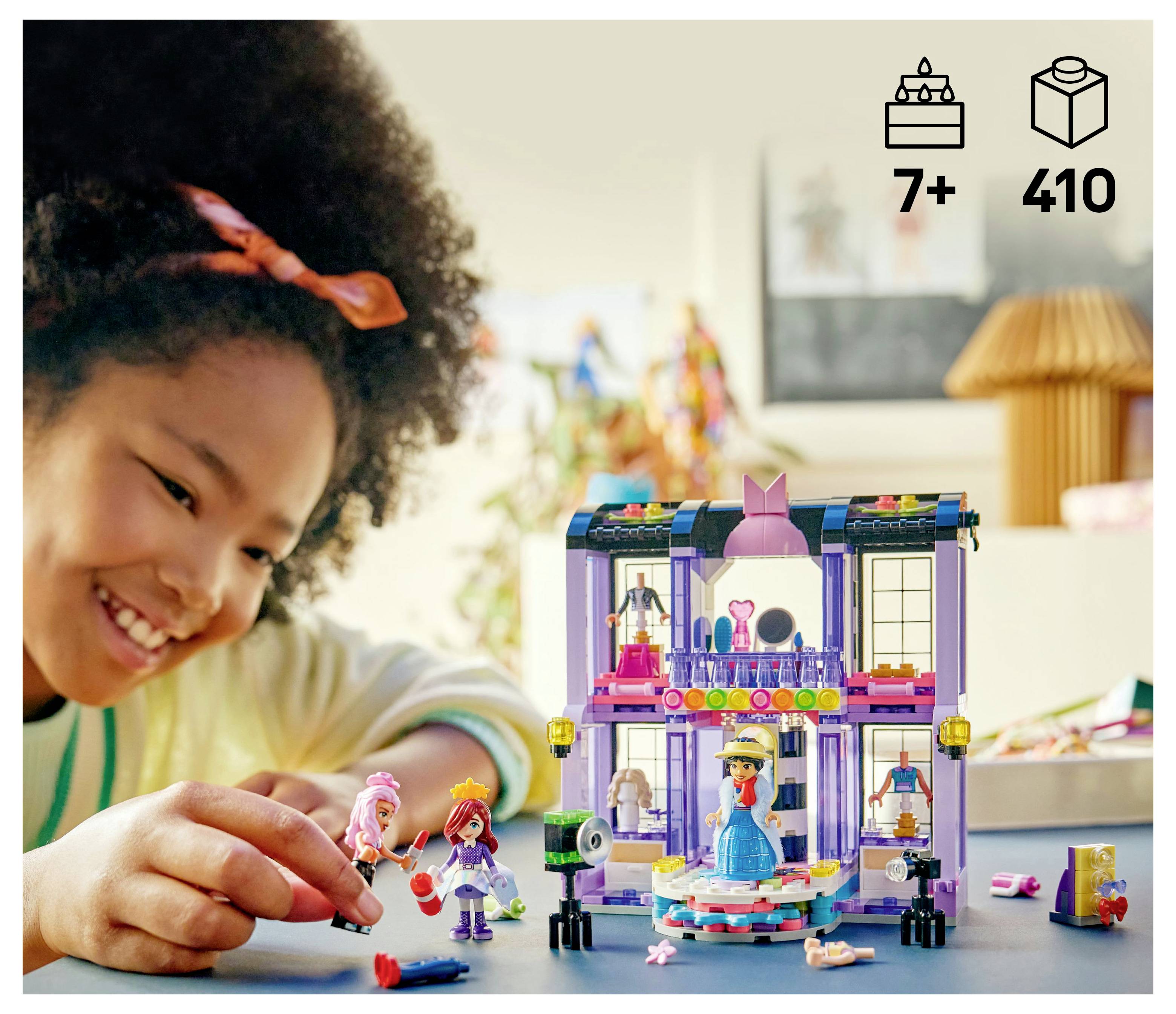 A child plays with a colorful toy house set featuring miniature figures and accessories. The box indicates suitable for ages 7 and up, with 410 pieces.