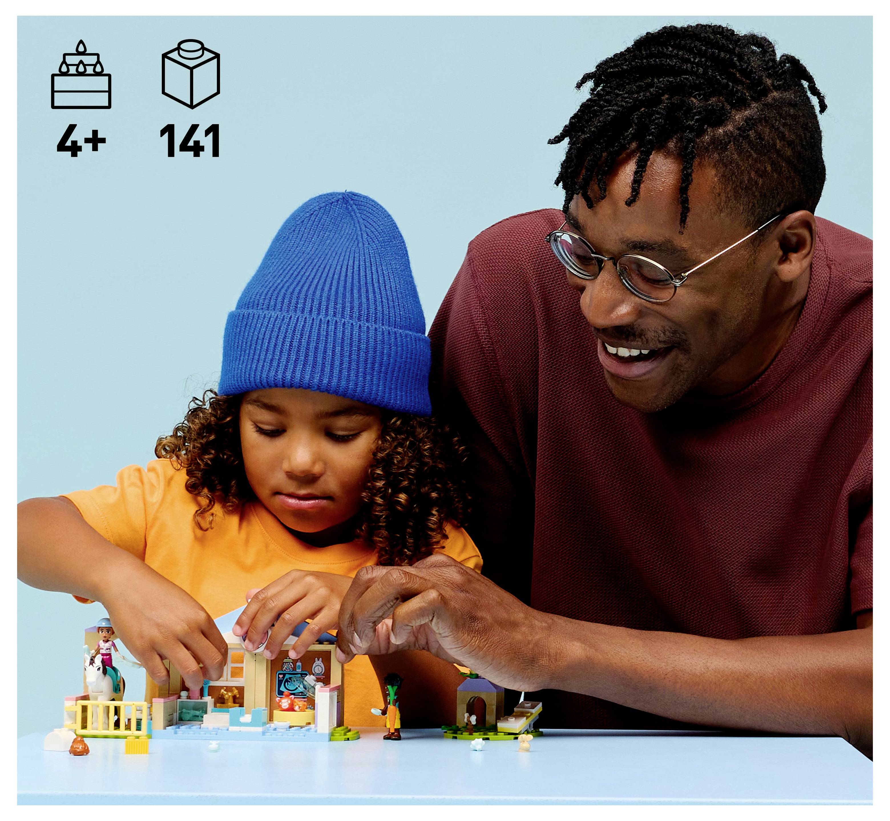 A child and an adult are building a small toy structure together. The toy is colorful and includes small figures. Icons show age 4+ and 141 pieces.