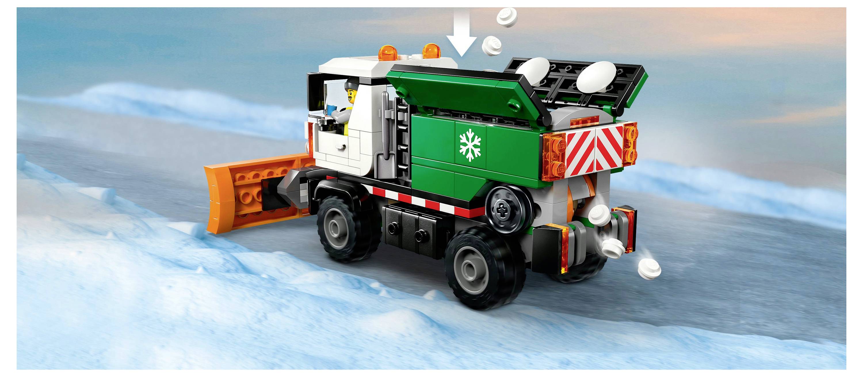 A toy snow plow truck on a snowy road dispenses snowballs. The truck is green and white with an orange plow on the front.