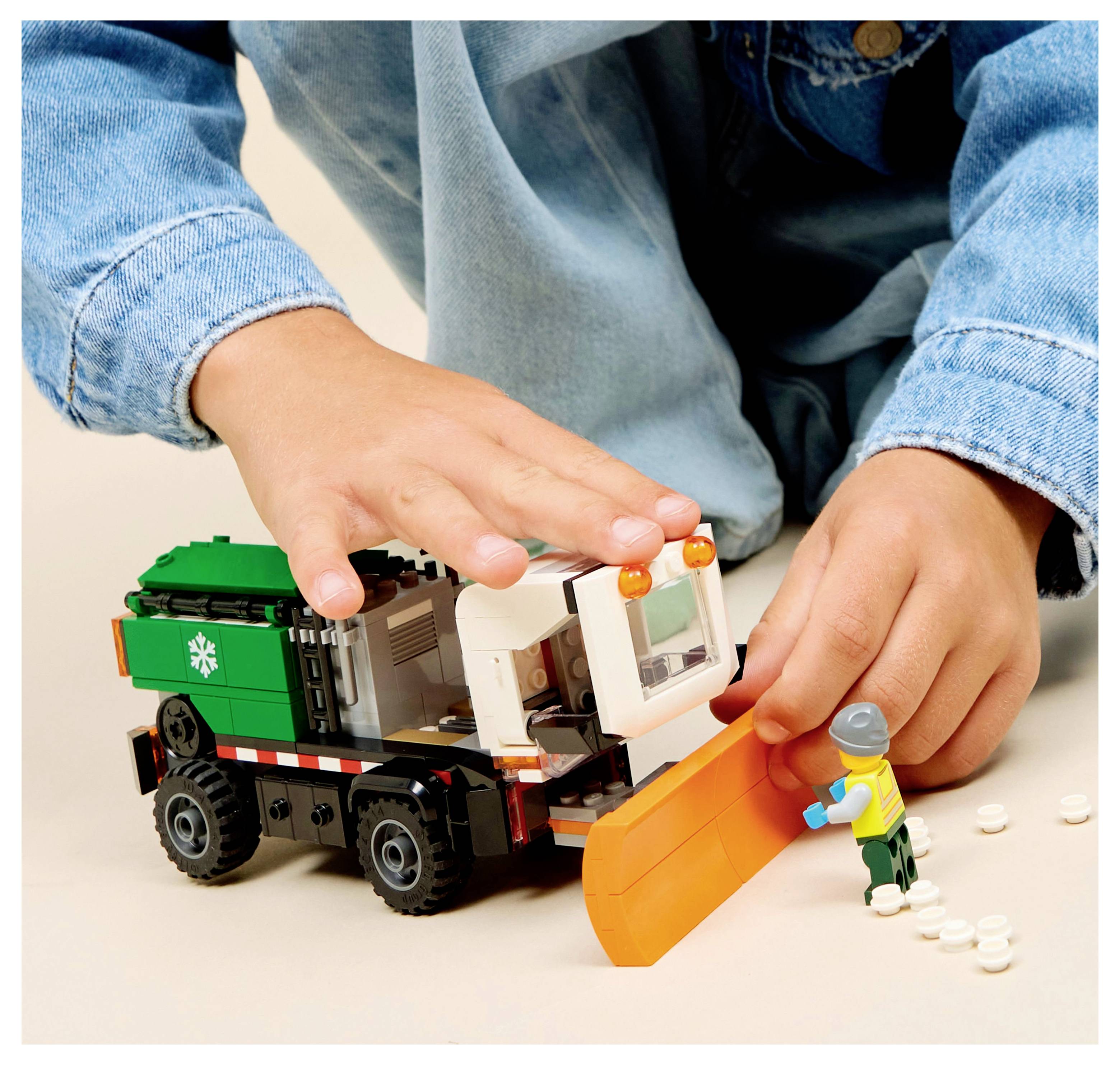 A child plays with a toy snowplow and a small figure, showcasing imaginative play and construction-themed toys.