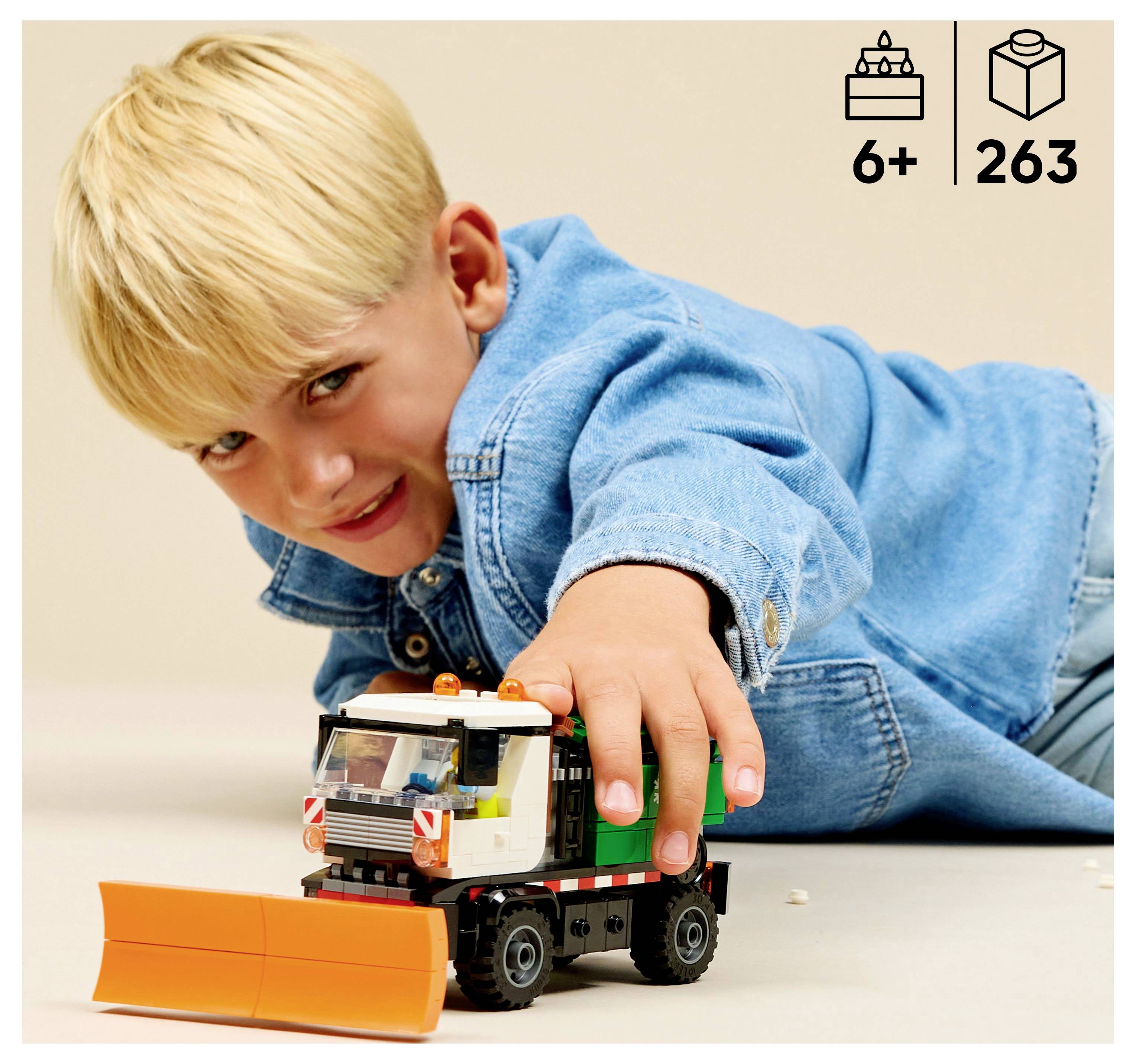 A child plays with a toy construction truck featuring a snowplow. Icons indicate it's suitable for ages 6+ and contains 263 pieces.