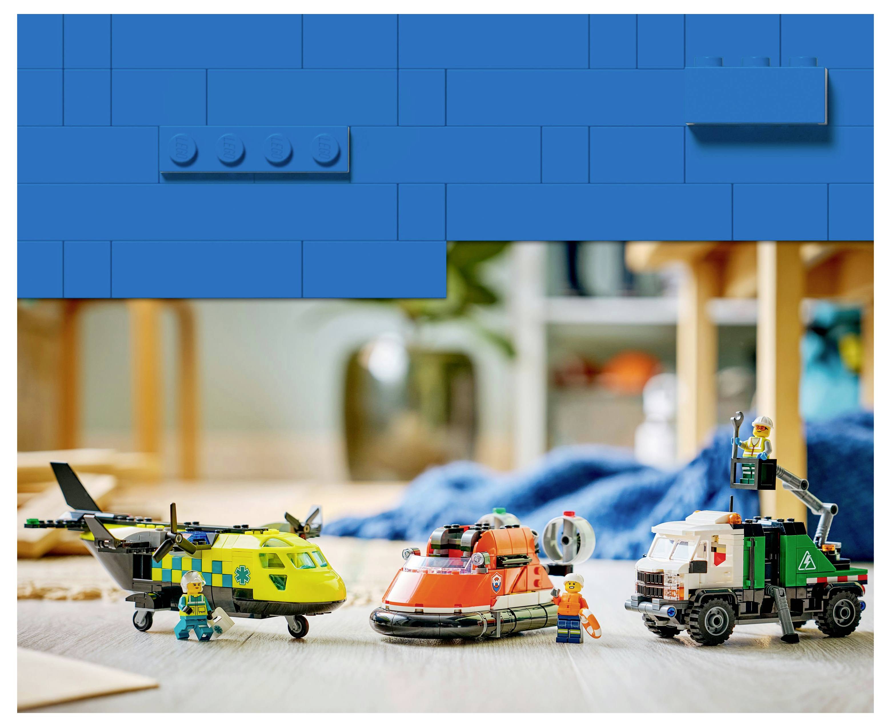 Toy construction scene with a helicopter, hovercraft, and truck, each with figures in uniforms. Blue LEGO block border above.