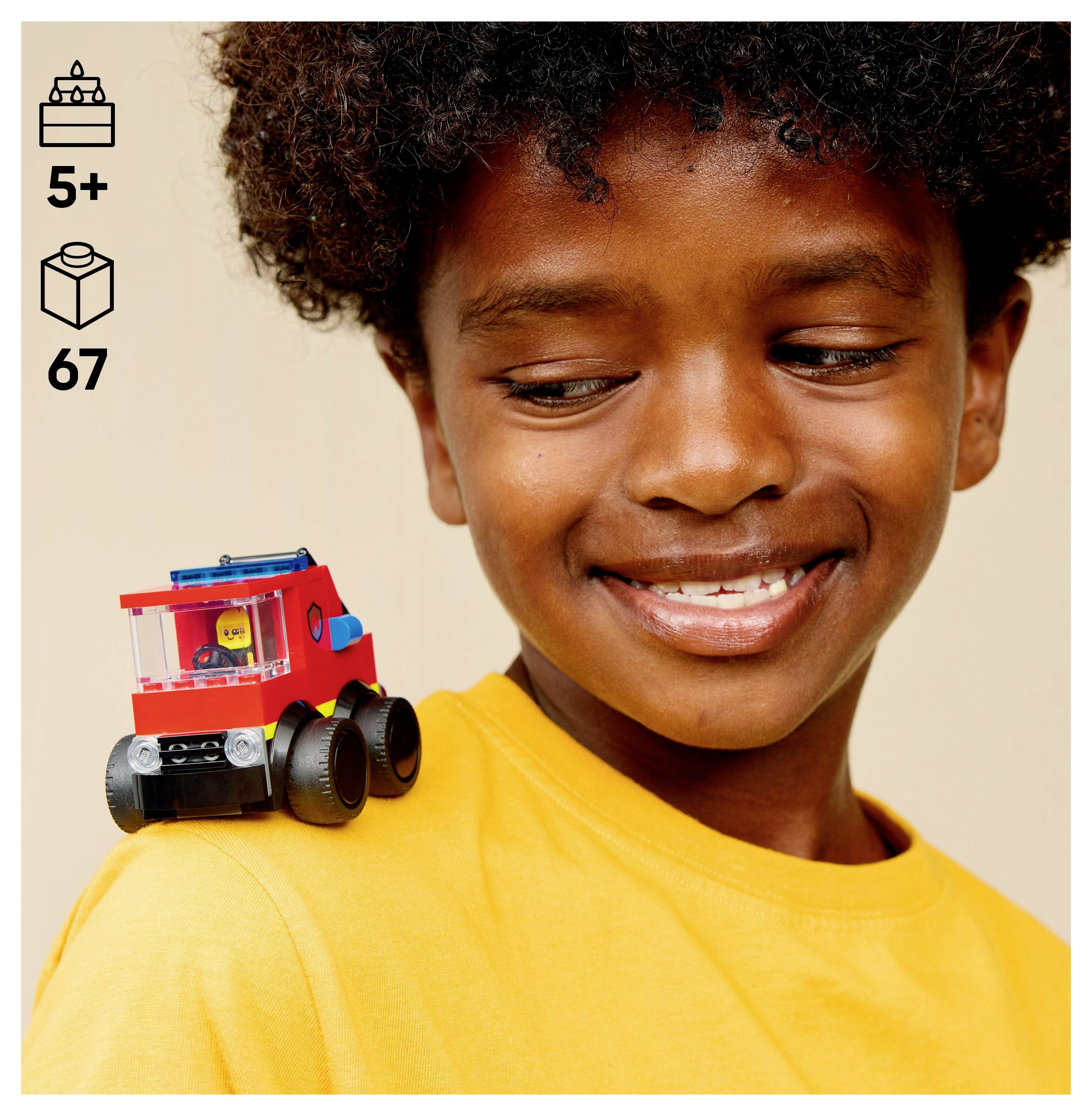 A smiling child in a yellow shirt with a small toy vehicle on their shoulder. Icons on the left indicate ages 5+ and 67 pieces.