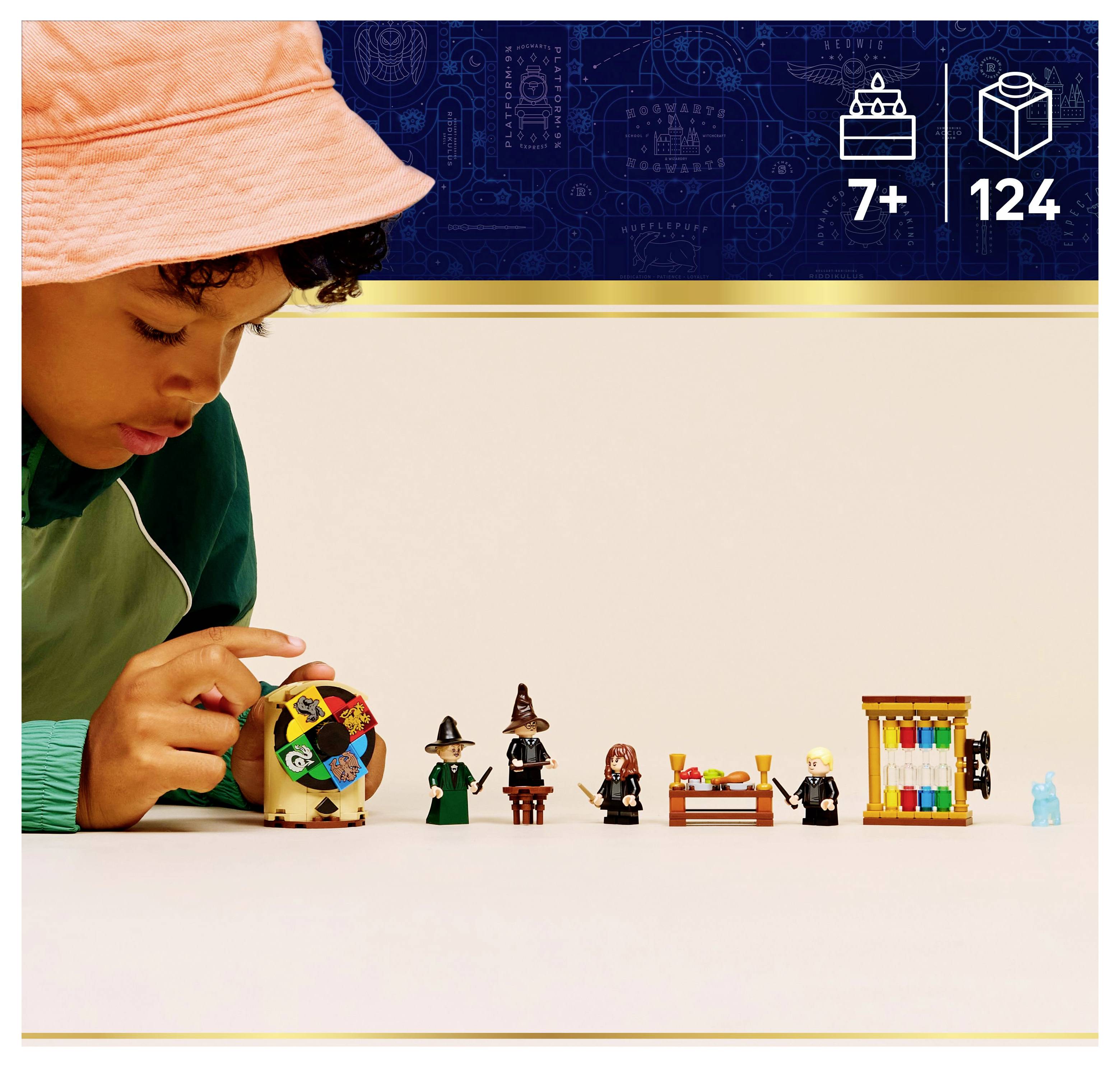 A child in a pink hat plays with a set of small toy figures and objects, including a spinning top and characters in wizard attire. The image includes a label for 7+ age and 124 pieces.