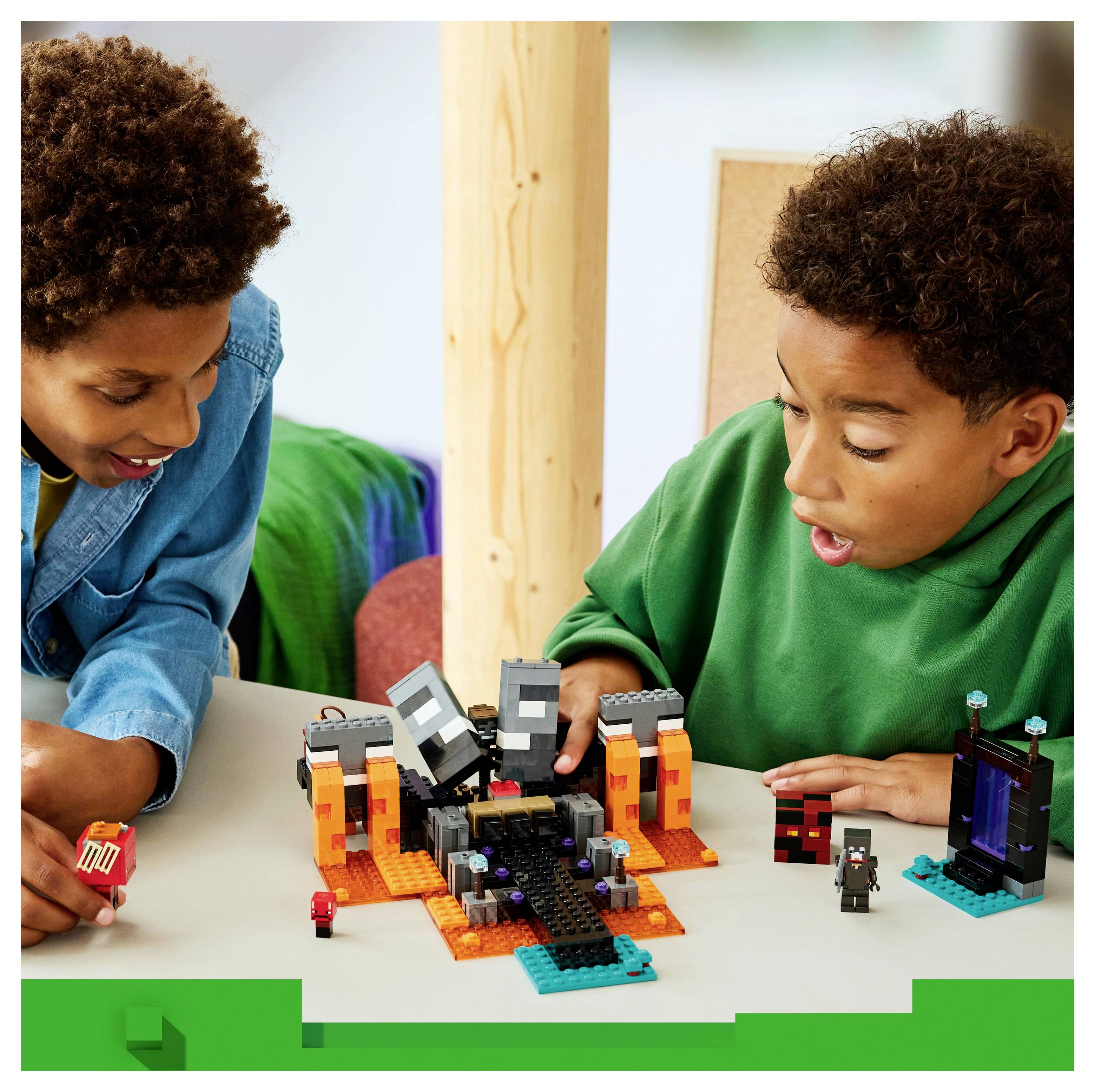Two children are engaged in building and playing with a block set on a table, featuring a miniature portal and characters.