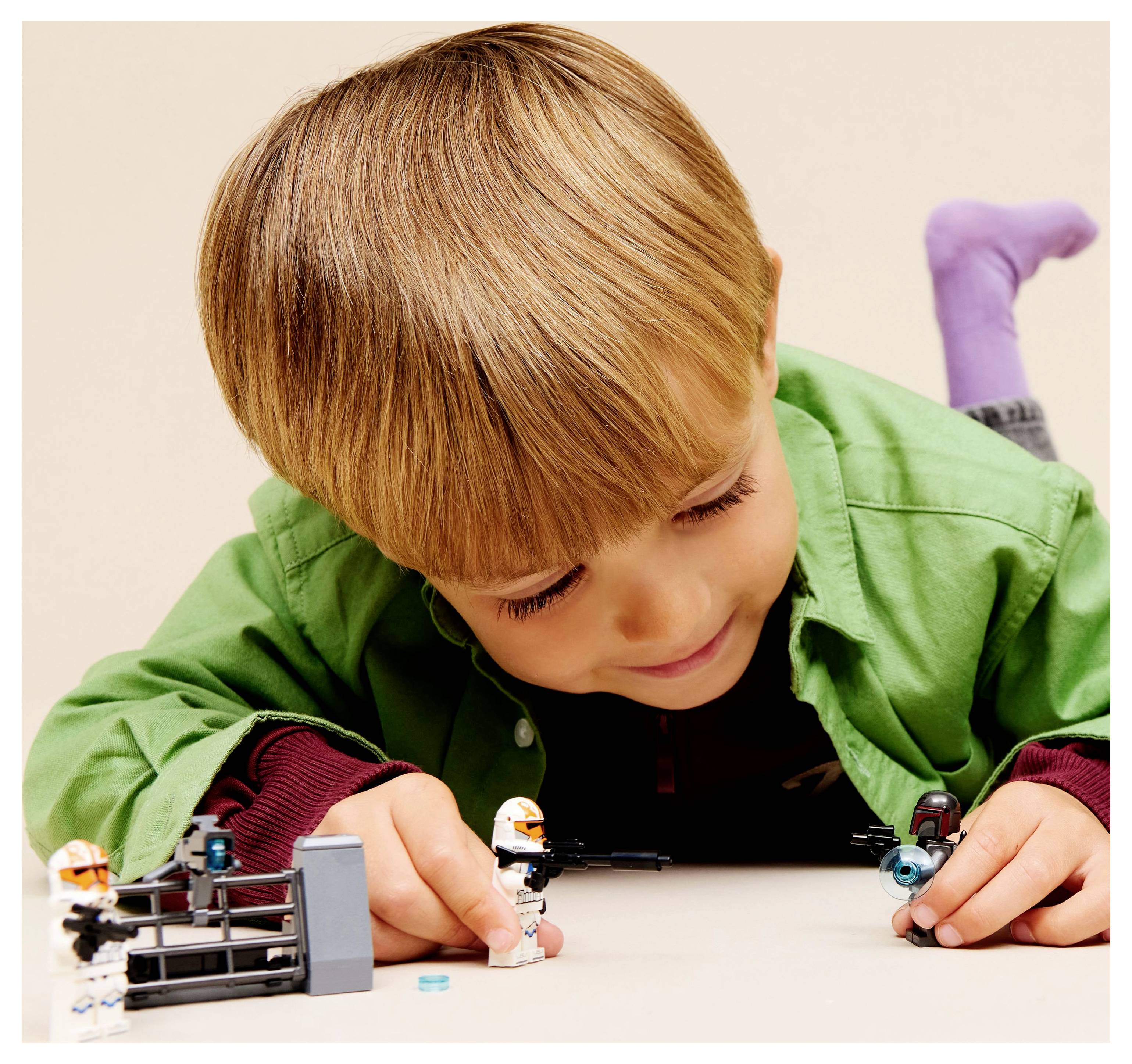 A child in a green shirt lies on the floor, focused on playing with LEGO figures and accessories, demonstrating imaginative play.