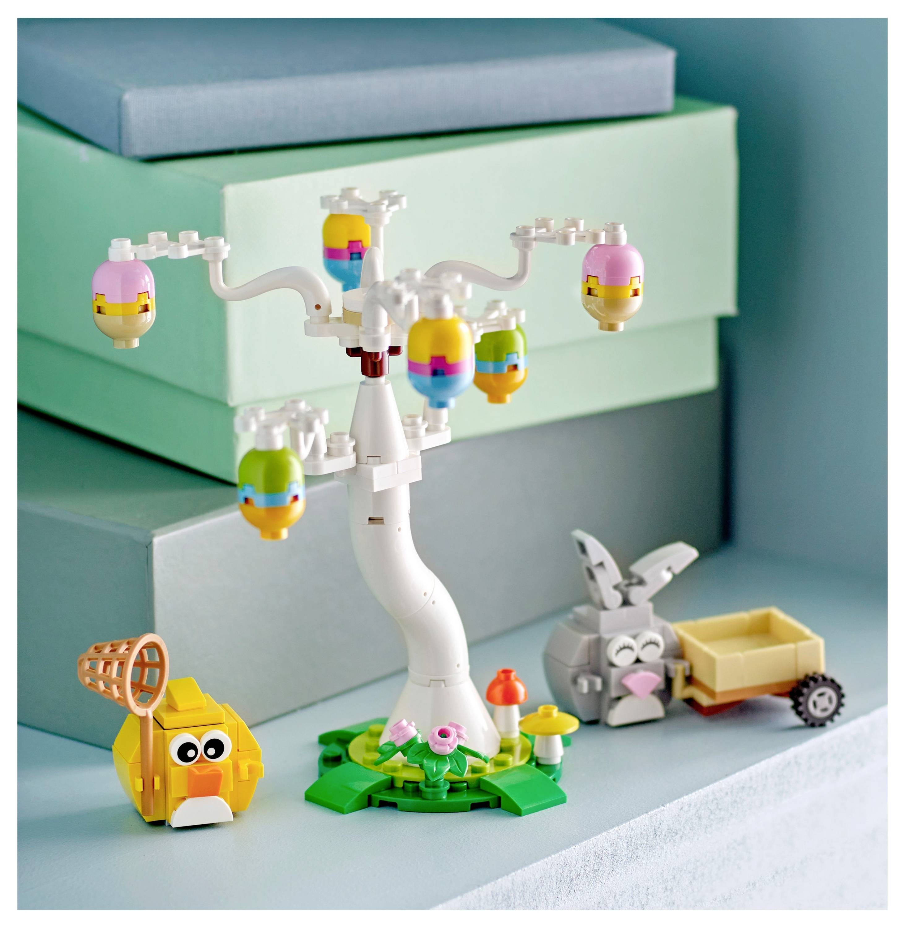A whimsical scene with colorful toy blocks forming a tree, a bunny, a wagon, and a round bird, set against a teal and blue background.