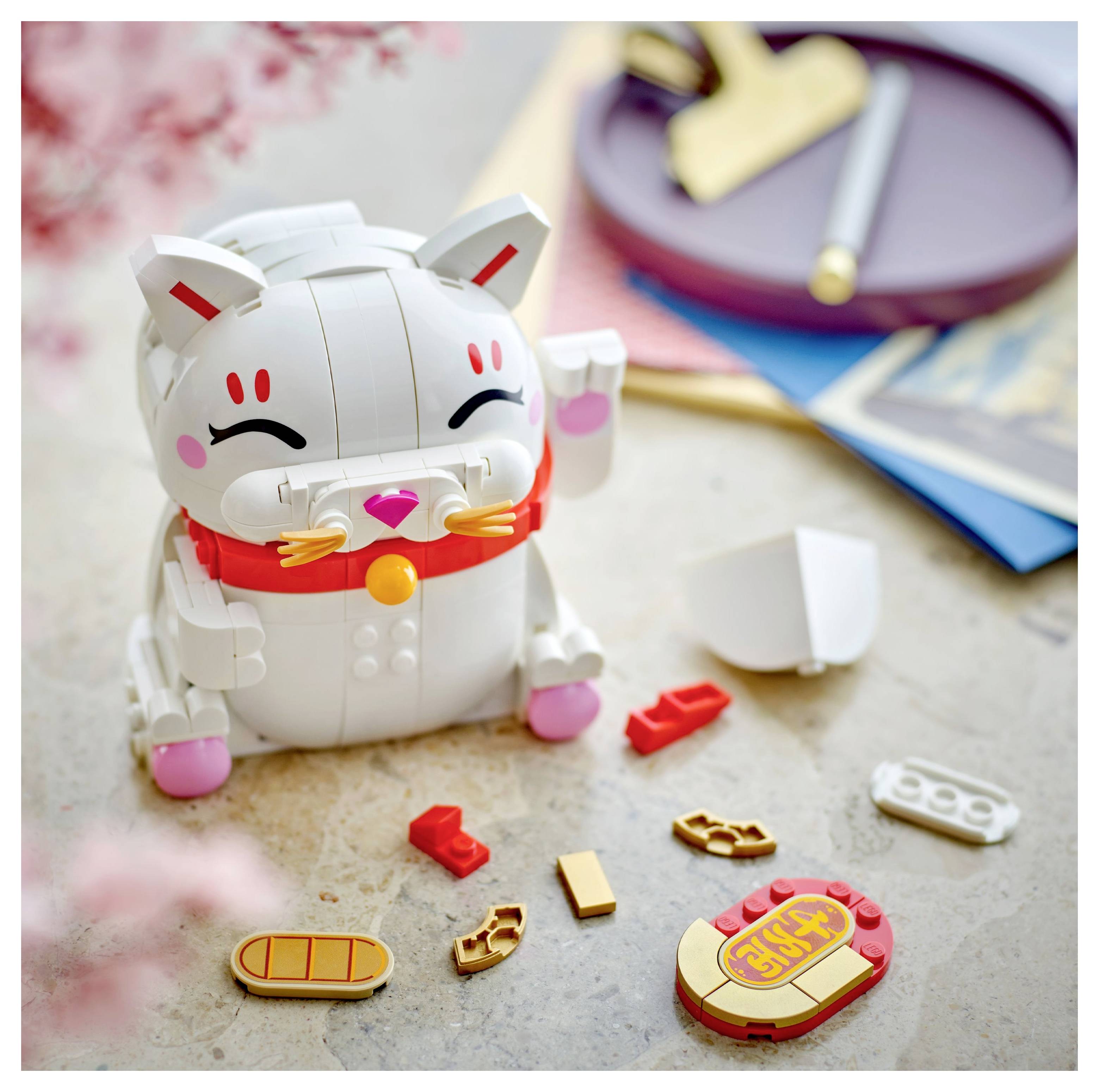 A toy cat assembly kit featuring a smiling white cat with red markings and various parts scattered around, including paws and a bell.