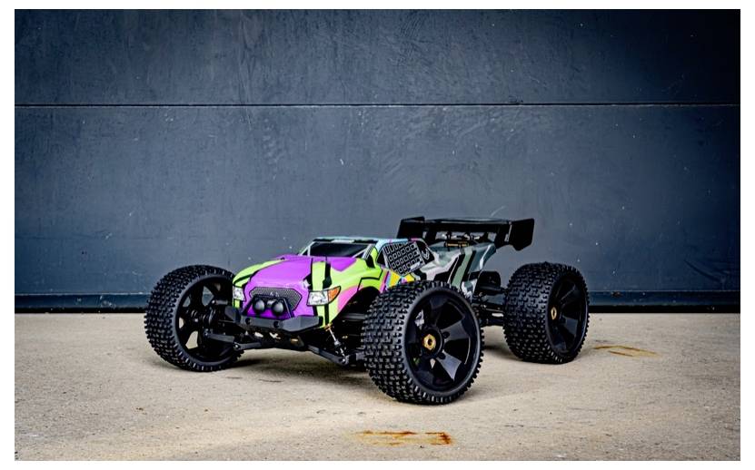 A colorful remote-controlled off-road car with large tires and a spoiler, parked on a concrete floor against a dark gray wall.