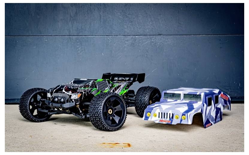 A remote-controlled car with a rugged, exposed design sits next to a blue and white camouflage car shell on a concrete surface.