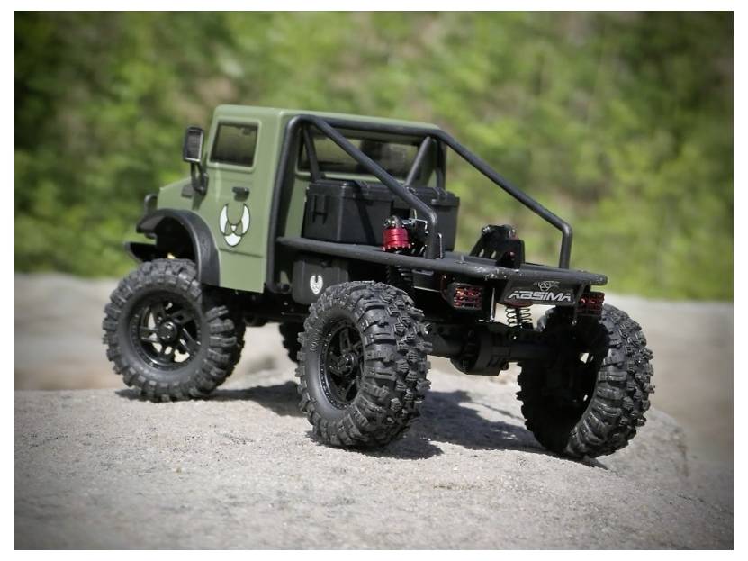 A rugged remote-controlled off-road vehicle with large tires, green body, and noticeable suspension, positioned on rocky terrain outdoors.