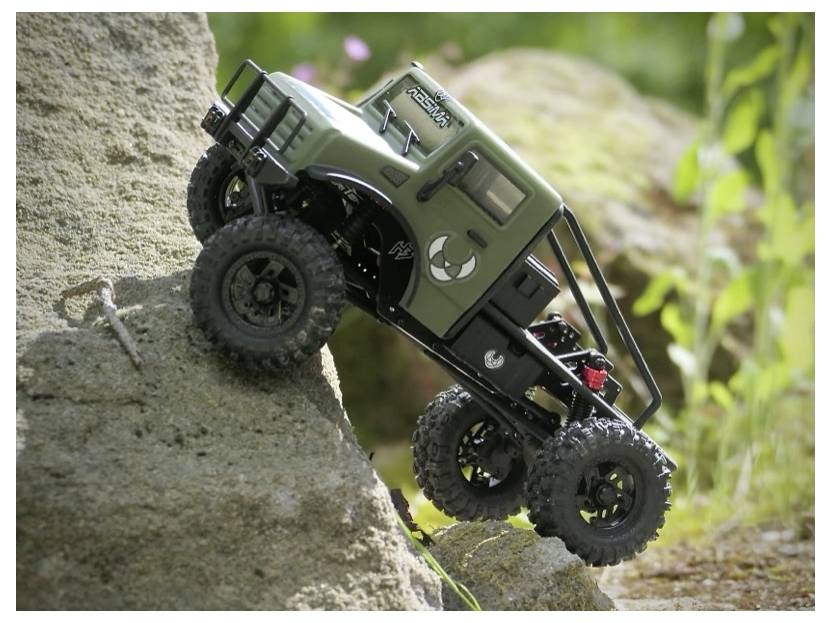 A green remote-controlled off-road vehicle climbs a large rock in a natural outdoor setting, showcasing its rugged design and suspension.