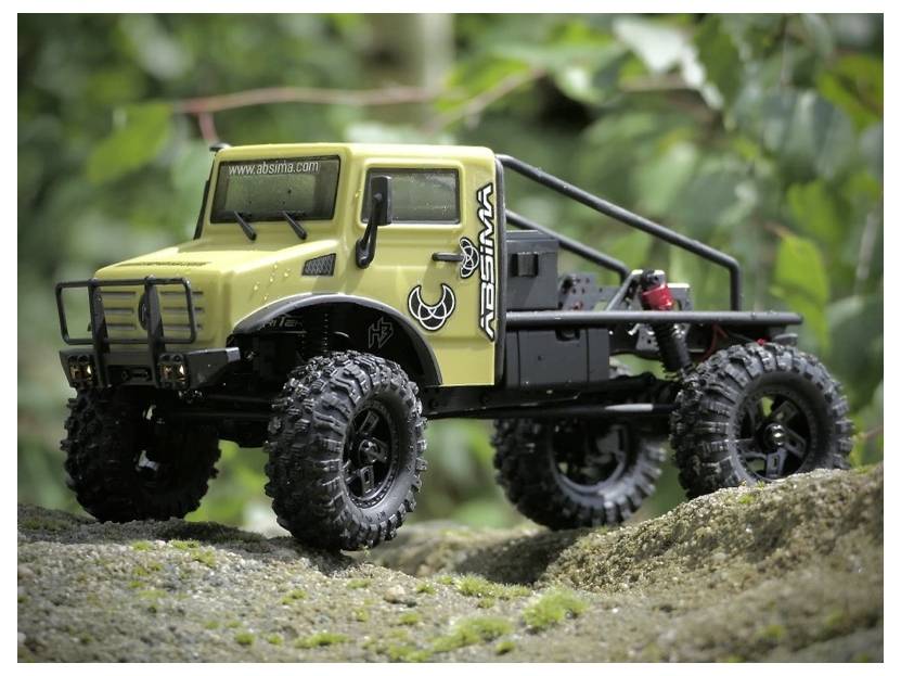 A yellow and black off-road truck model on rocky terrain, surrounded by greenery, showcasing its rugged build and large tires.