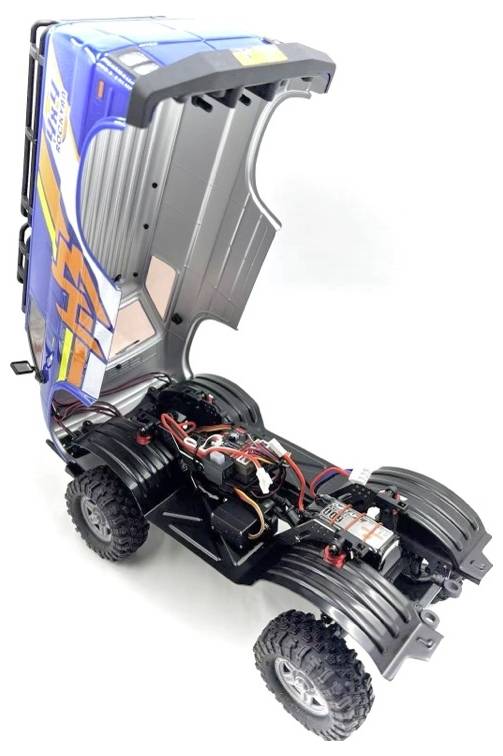 A remote-controlled truck with its blue and orange cover lifted, exposing the internal wiring and components. The truck has large, rugged tires.
