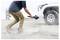 A person captures video footage close to the ground using a handheld camera gimbal next to a parked vehicle in a dusty outdoor setting.