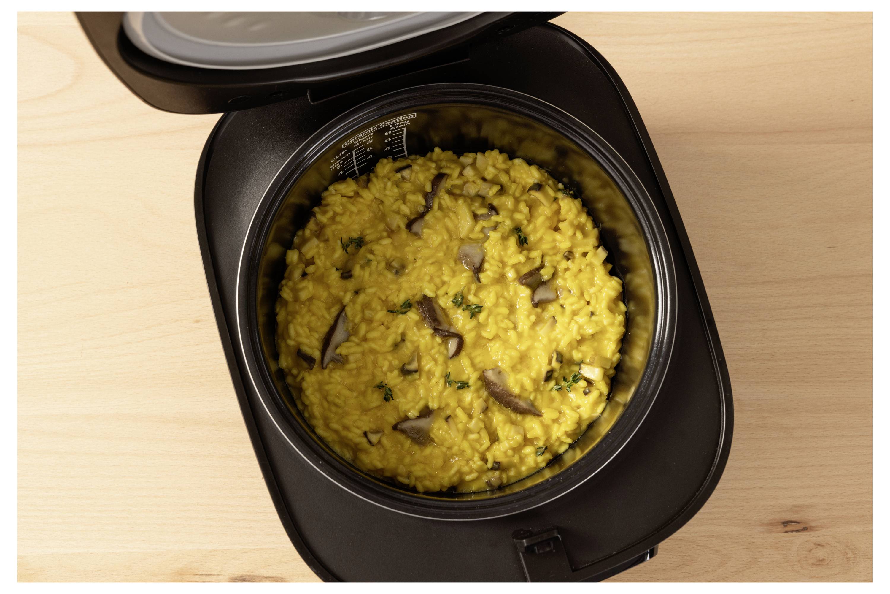 Rice cooker filled with yellow mushroom risotto, seen from above, on a wooden countertop.