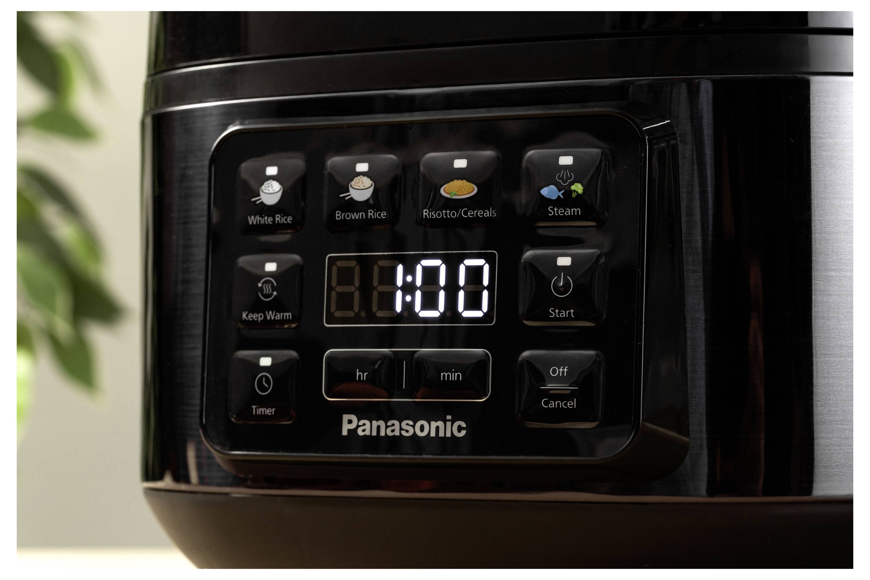 A close-up of a Panasonic rice cooker control panel, displaying a digital timer set to 1:00. Various function buttons are visible.