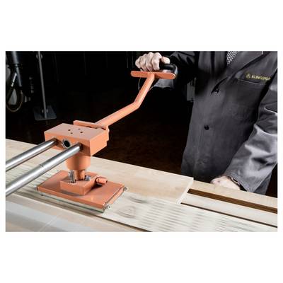 A person in a workshop uses an orange manual press on a wooden surface, likely for clamping or pressing activities.
