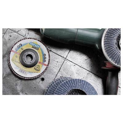 A close-up of a textured, circular abrasive disc labeled 'SMT 624' lies on a concrete floor next to a green handheld power tool.